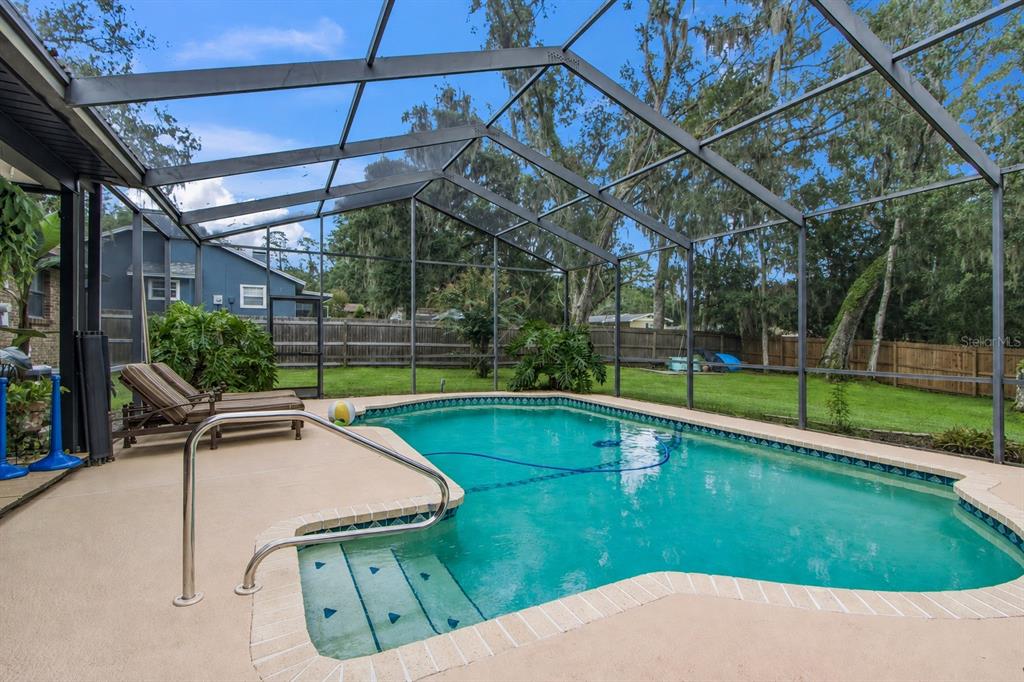 A screened-in swimming pool with a concrete deck and lounge chairs in a backyard — 527 COLONIAL DRIVE, BROOKSVILLE, FL