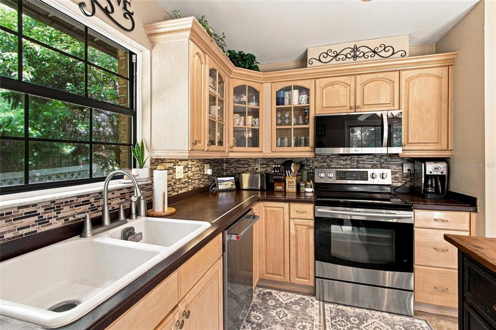 A kitchen features light wood cabinets, dark countertops, stainless steel appliances, and a tiled backsplash — 527 COLONIAL DRIVE, BROOKSVILLE, FL