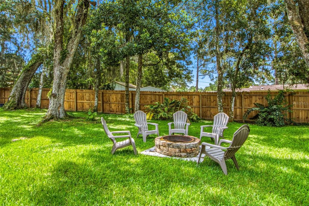 A backyard features a stone fire pit surrounded by four chairs on a grassy lawn — 527 COLONIAL DRIVE, BROOKSVILLE, FL