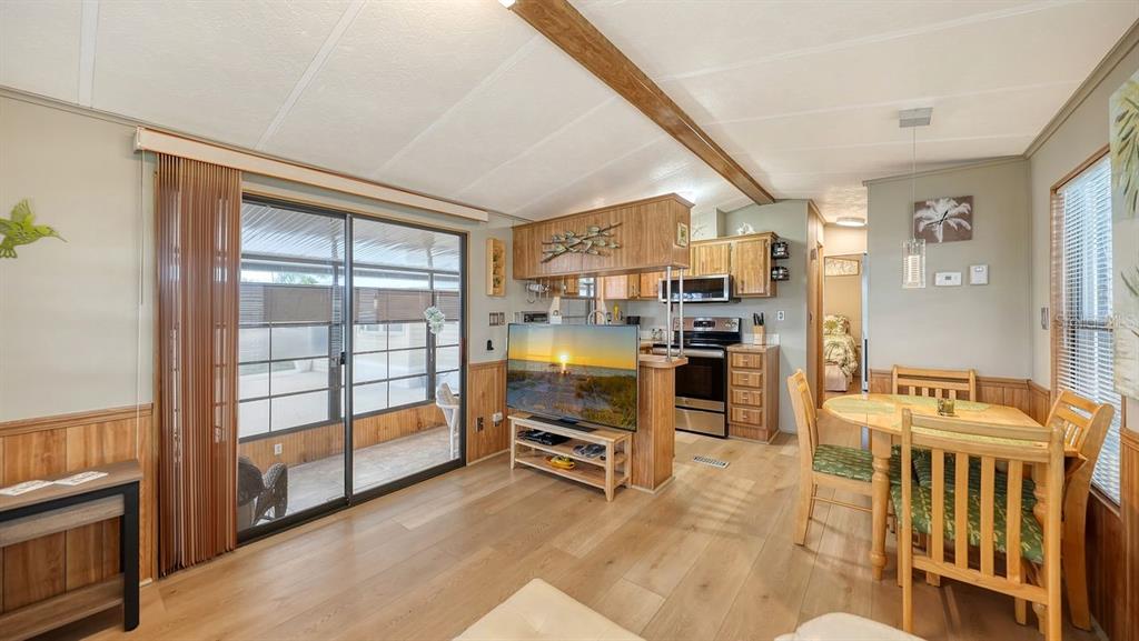 An open-concept living and dining area features wood-paneled walls, light wood flooring, and sliding doors — 1475 FLAMINGO DRIVE UNIT 71, ENGLEWOOD, FL