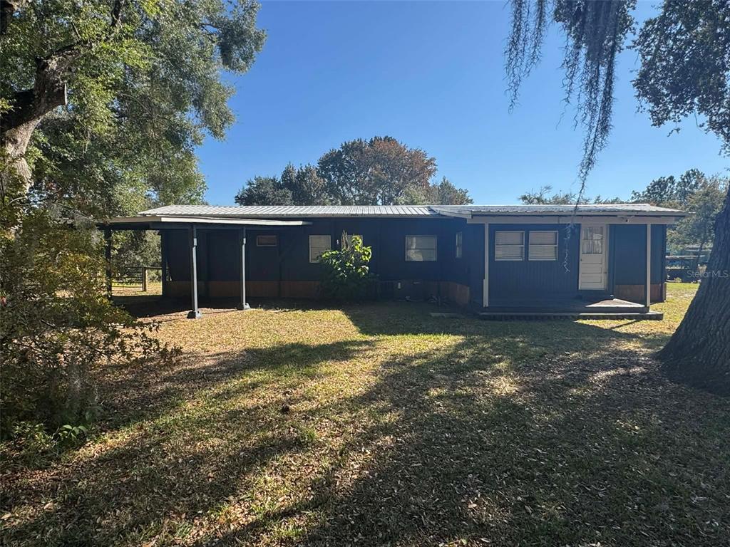 A dark-painted mobile home with a metal roof and a covered porch sits on grass — 21162 NE 146TH PLACE, SALT SPRINGS, FL