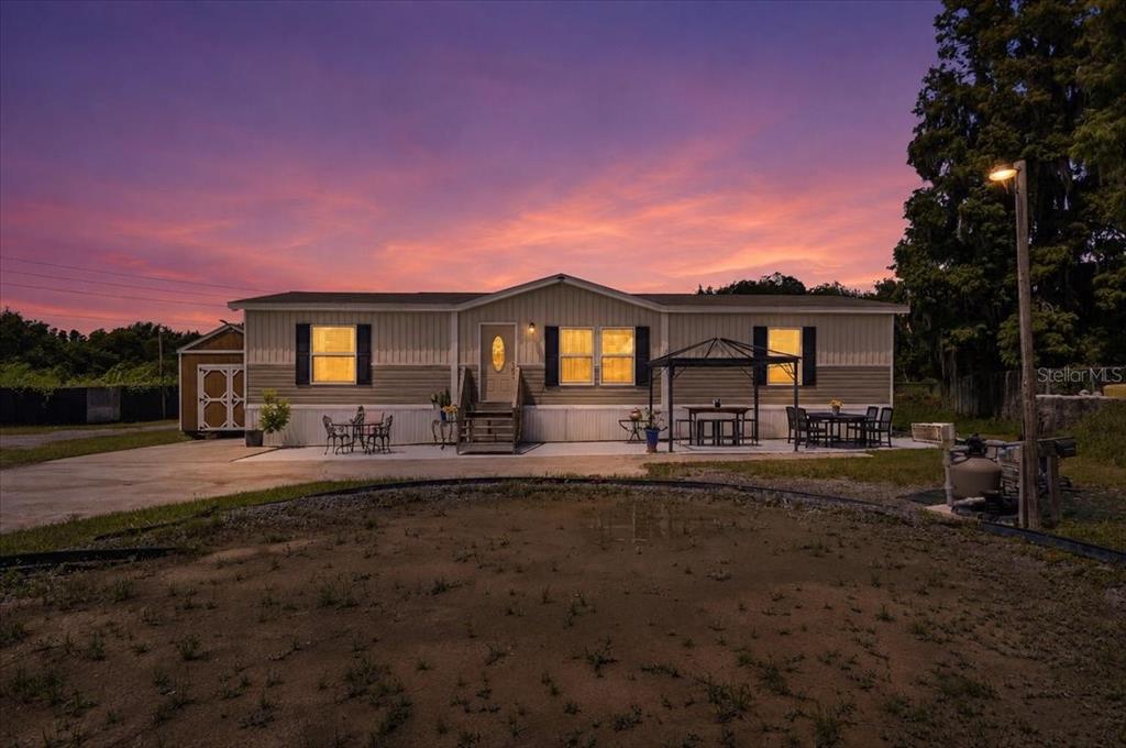 A single-story manufactured home with a concrete patio and a sunset sky in the background — 2531 DAWN HEIGHTS DRIVE, LAKELAND, FL