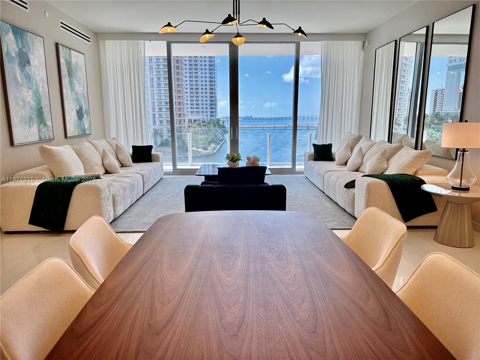 A dining area overlooks a living room with two white sofas and a waterfront view — 300 Biscayne Blvd Way # 503C, Miami FL 33131, MIAMI, FL