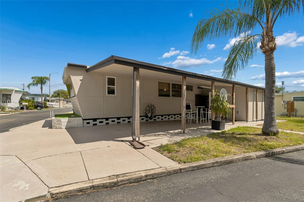 A single-story mobile home features a covered carport and a palm tree in the yard — 1915 SEMINOLE BOULEVARD UNIT 140, LARGO, FL