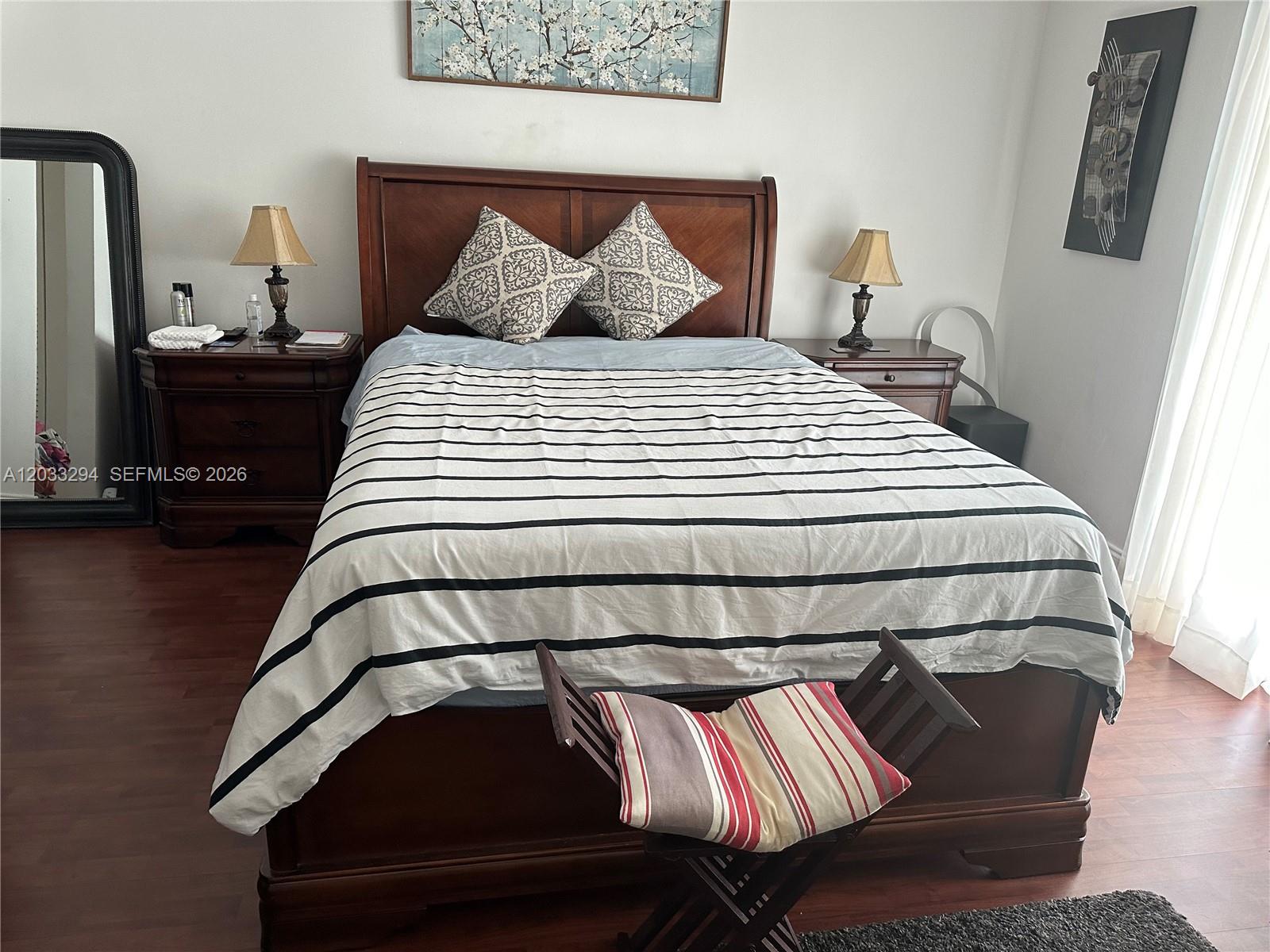 A bedroom features a wooden bed frame, two nightstands with lamps, and a striped comforter — 1610 Lenox Ave # 412, Miami Beach FL 33139, MIAMI BEACH, FL