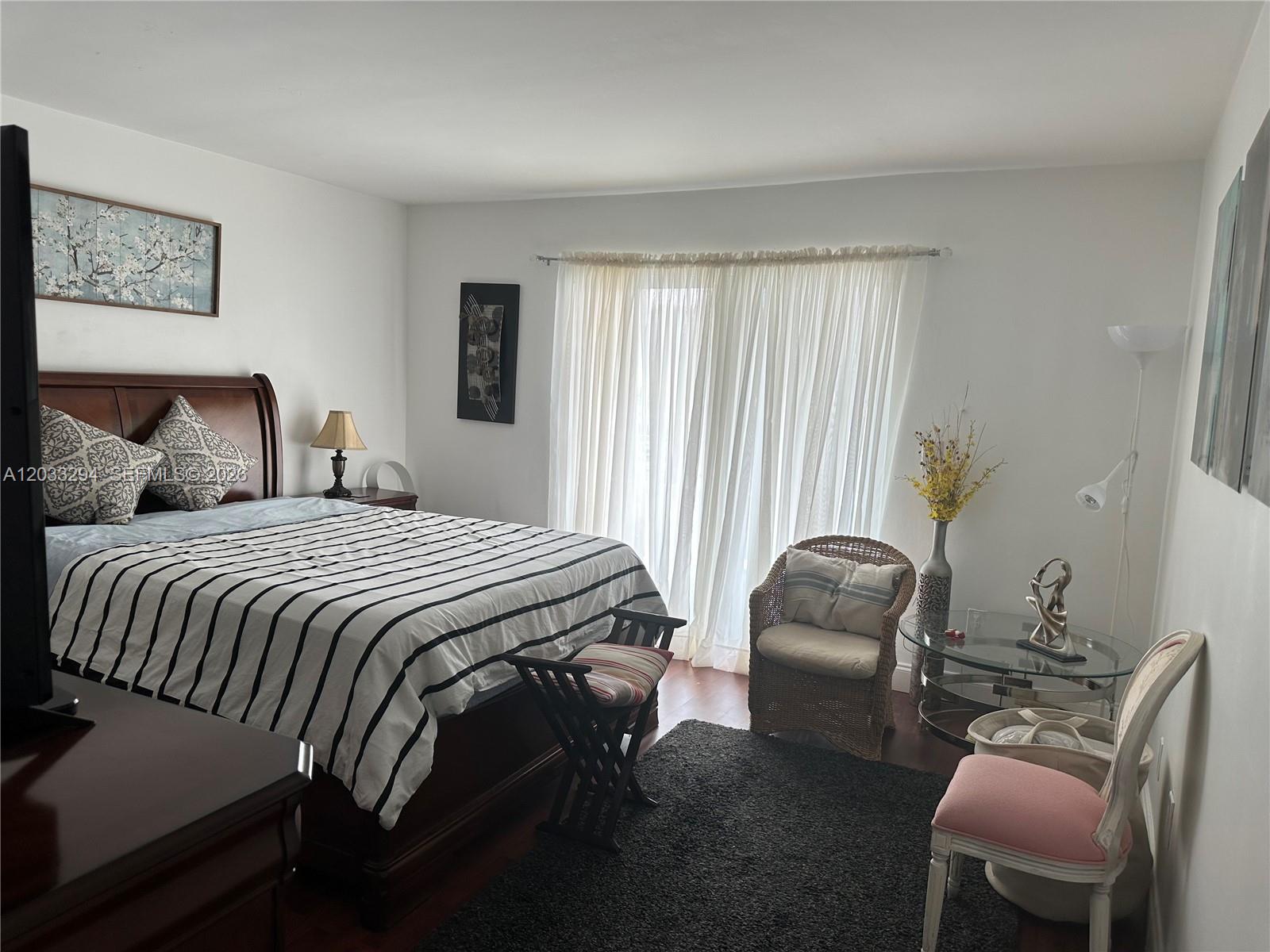 A bedroom features a wooden bed with striped bedding, a wicker chair, and a glass table — 1610 Lenox Ave # 412, Miami Beach FL 33139, MIAMI BEACH, FL