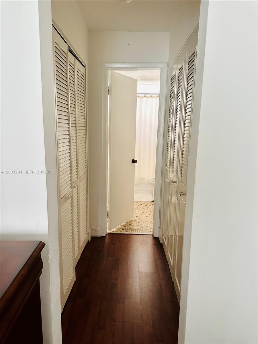 A narrow hallway with wood-look flooring leads to a bathroom with louvered closet doors — 1610 Lenox Ave # 412, Miami Beach FL 33139, MIAMI BEACH, FL