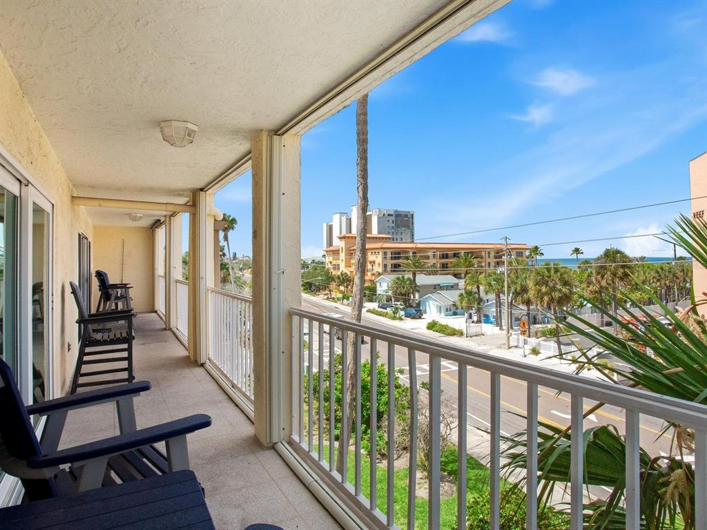 A balcony with chairs overlooks a street, palm trees, and the ocean in the distance — 1005 GULF BOULEVARD UNIT 10, INDIAN ROCKS BEACH, FL