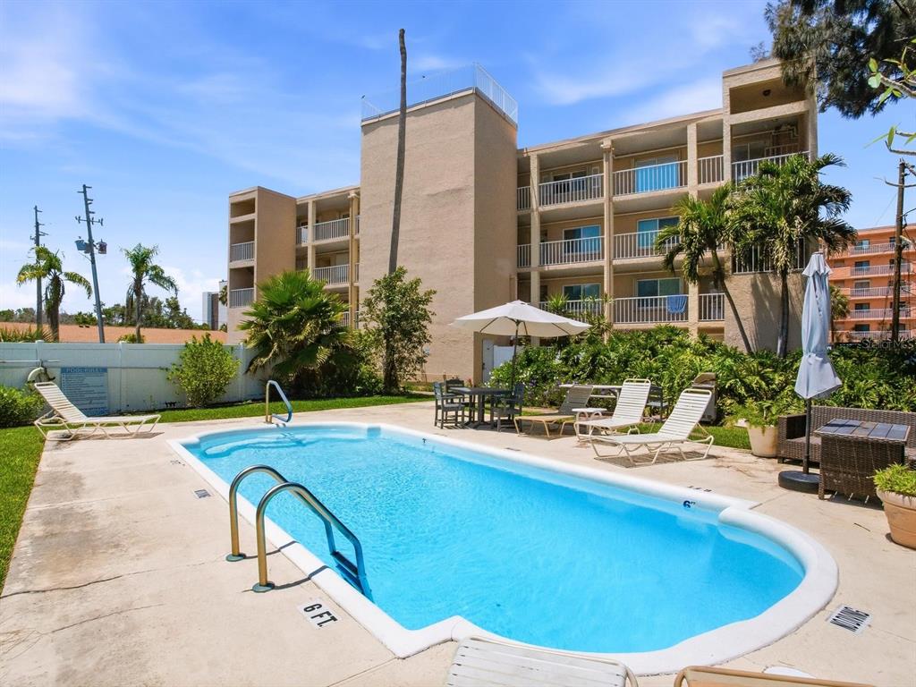 A swimming pool sits in front of a multi-story apartment building with palm trees — 1005 GULF BOULEVARD UNIT 10, INDIAN ROCKS BEACH, FL