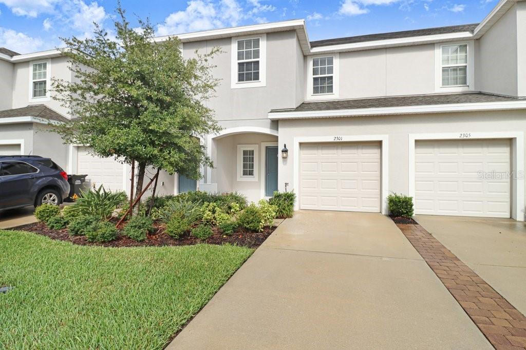 A two-story townhouse exterior features a beige facade, two garage doors, and a front lawn — 2301 ALEE LANE, WESLEY CHAPEL, FL