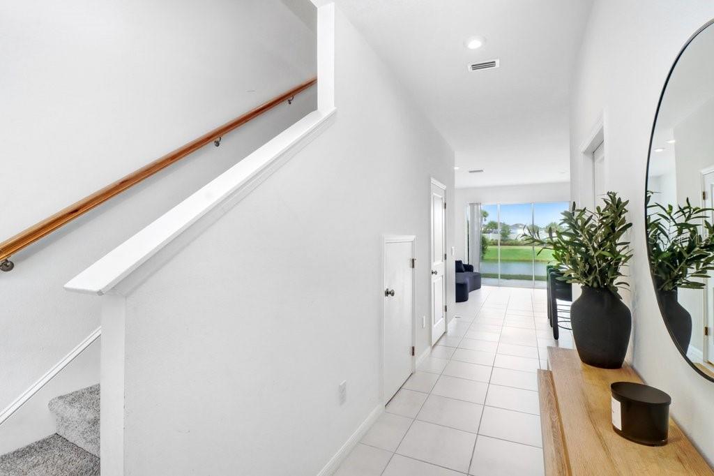 A bright hallway features white tile flooring, a staircase with a wooden railing, and a mirror — 2301 ALEE LANE, WESLEY CHAPEL, FL