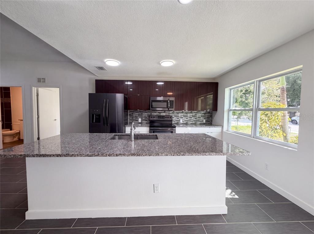 A kitchen features a granite-topped island, dark cabinetry, stainless steel appliances, and gray tile flooring — 2840 S SHADE AVENUE, SARASOTA, FL