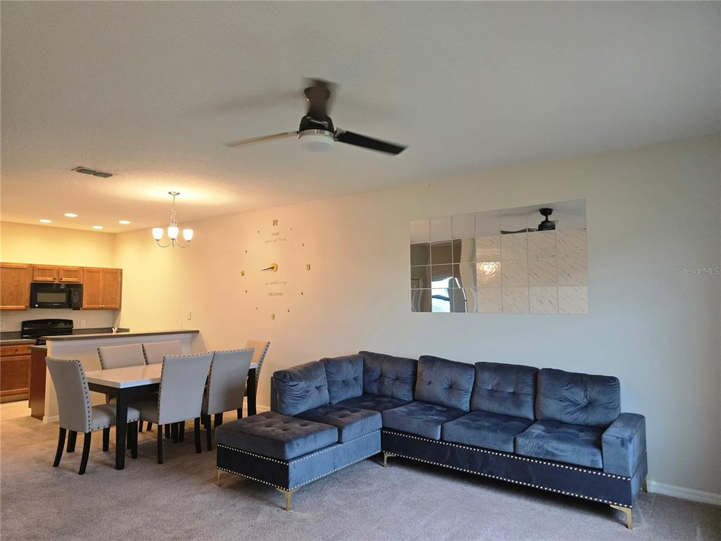 A living room with a blue sectional sofa, a dining area, and a wall clock — 1852 CORIANDER DR, POINCIANA, FL