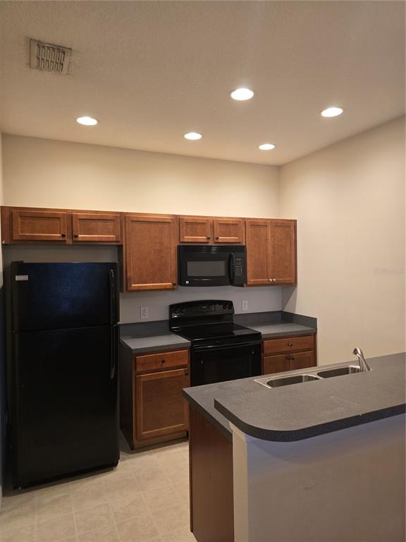 A kitchen features wood cabinets, black appliances, gray countertops, and recessed lighting — 1852 CORIANDER DR, POINCIANA, FL