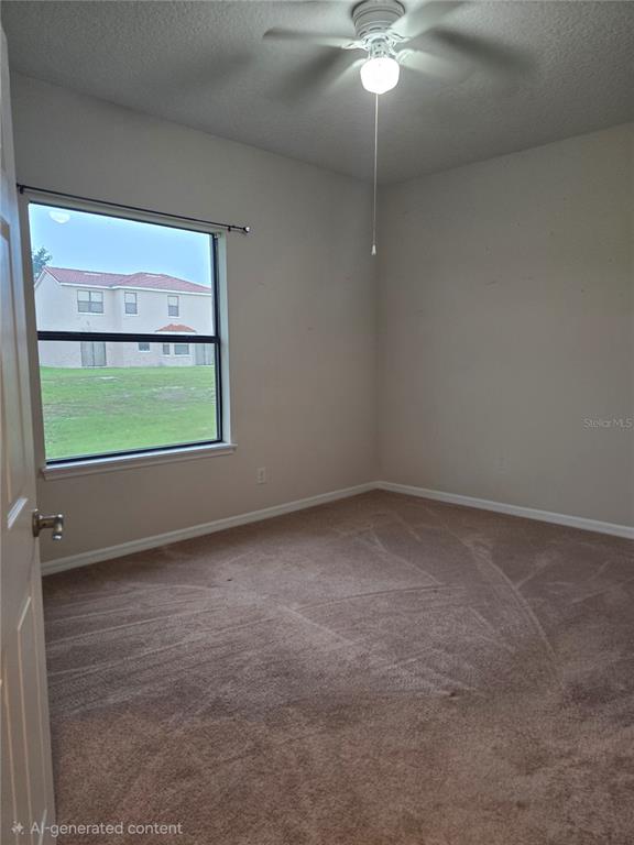 An empty bedroom features beige carpet, light-colored walls, a ceiling fan, and a window view — 1852 CORIANDER DR, POINCIANA, FL