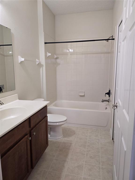 A bathroom features a white vanity, a toilet, and a shower-tub combination with white tiles — 1852 CORIANDER DR, POINCIANA, FL