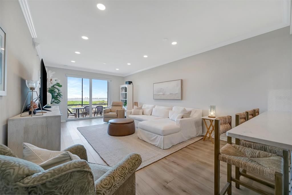 A bright living room features a white sectional sofa, light wood floors, and a balcony view — 850 TIDEWATER SHORES LOOP UNIT 105, BRADENTON, FL