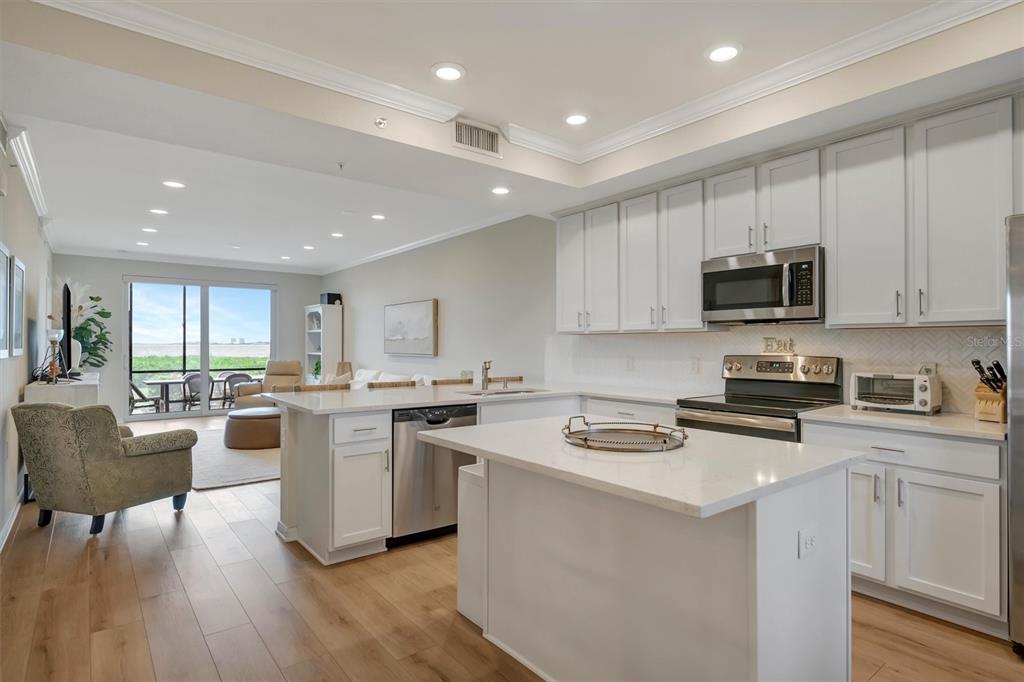 A modern kitchen with white cabinets and quartz countertops opens into a bright living area — 850 TIDEWATER SHORES LOOP UNIT 105, BRADENTON, FL