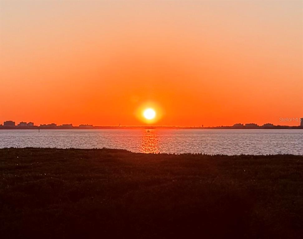 A vibrant orange sunset glows over a calm body of water with a distant shoreline — 850 TIDEWATER SHORES LOOP UNIT 105, BRADENTON, FL