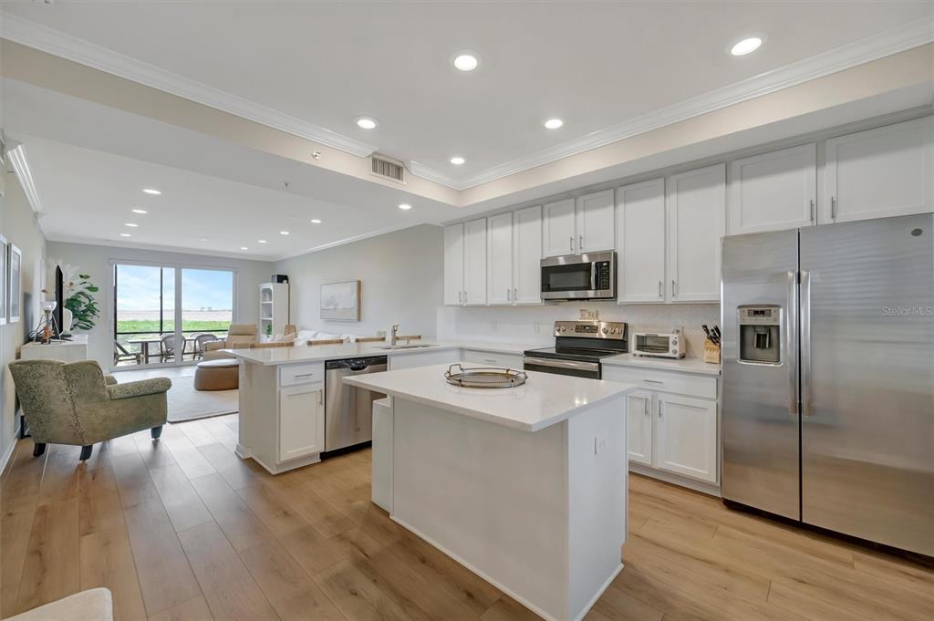 A modern kitchen with white cabinets, stainless steel appliances, and an island overlooks a living area — 850 TIDEWATER SHORES LOOP UNIT 105, BRADENTON, FL