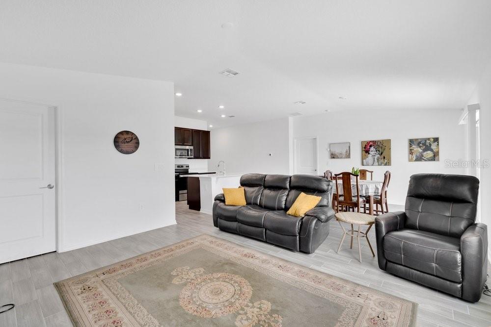 A living room with gray tile floors, a black leather sofa, and an open kitchen — 839 OFANTO WAY, HAINES CITY, FL