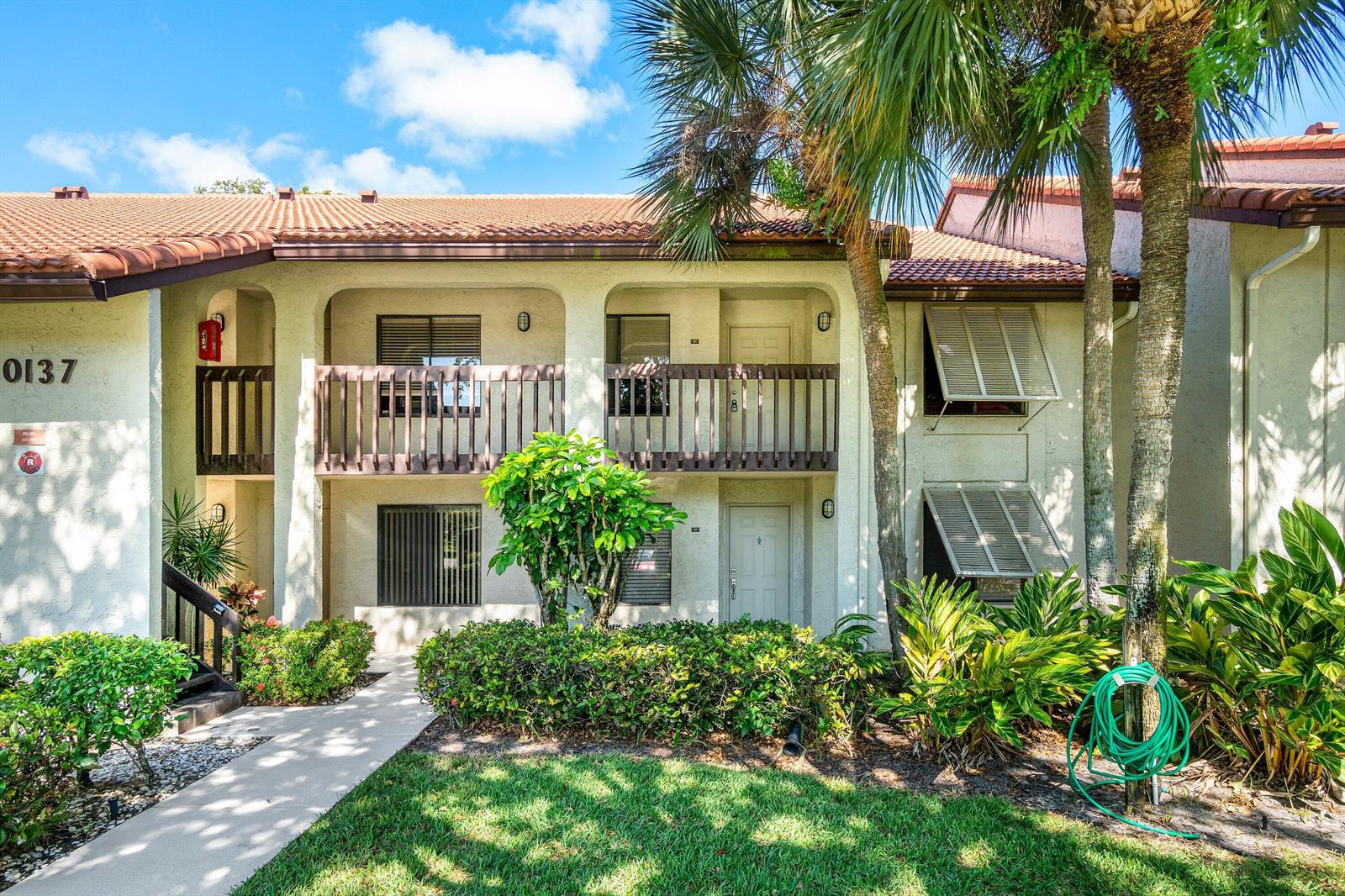 A two-story apartment building with a tiled roof, balconies, and lush landscaping in front — 10137 Mangrove Drive # 203, Boynton Beach FL 33437, BOYNTON BEACH, FL