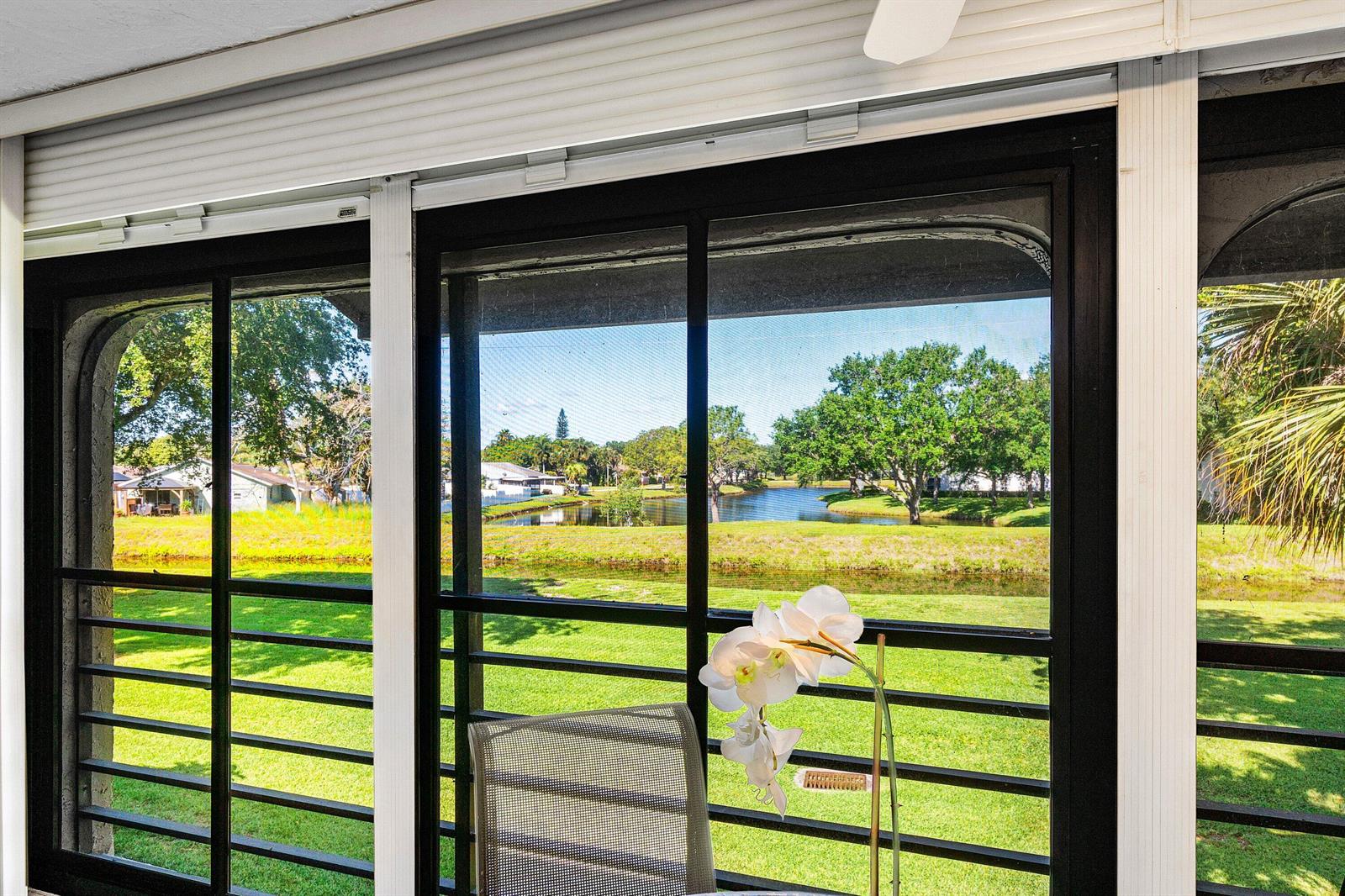 A view of a grassy lawn and pond seen through a screened-in porch window — 10137 Mangrove Drive # 203, Boynton Beach FL 33437, BOYNTON BEACH, FL