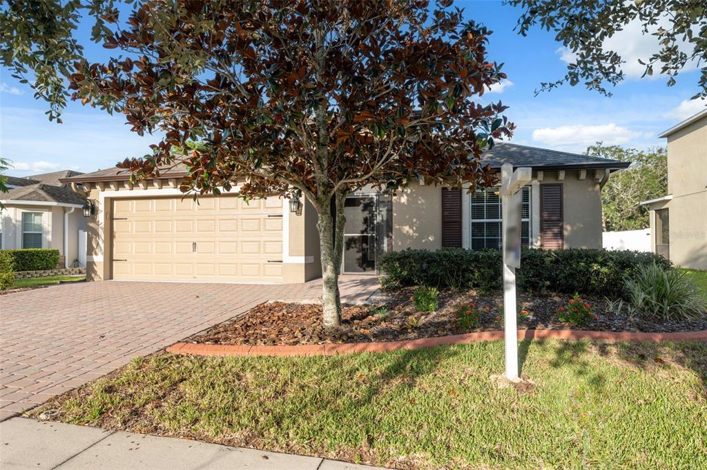 A single-story house with a tan exterior, a two-car garage, and a large front tree — 18035 ARBOR CREST DRIVE, HUDSON, FL