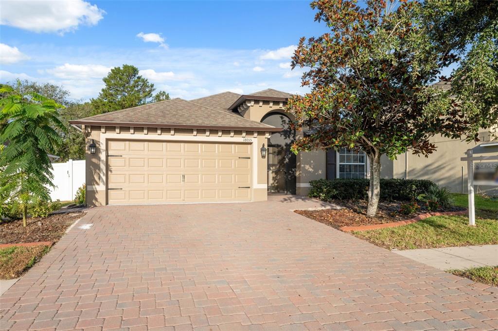 A single-story house with a tan stucco exterior, a two-car garage, and a paved driveway — 18035 ARBOR CREST DRIVE, HUDSON, FL
