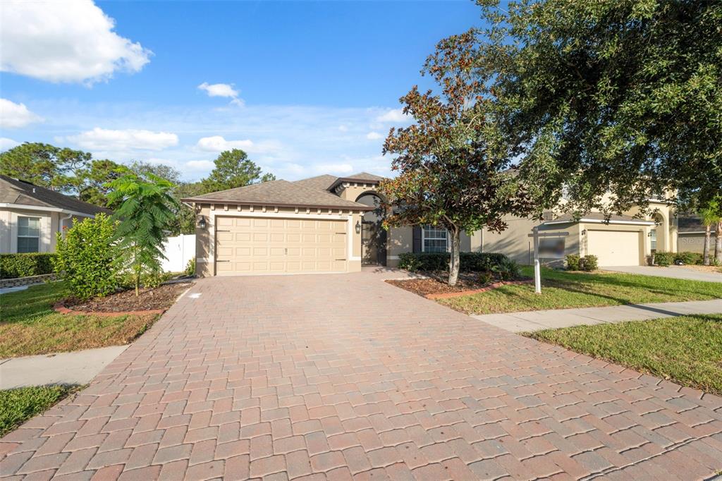 A single-story house with a tan garage and a brick paver driveway under a blue sky — 18035 ARBOR CREST DRIVE, HUDSON, FL