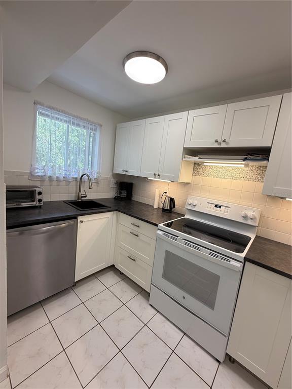 A kitchen features white cabinets, dark countertops, a stainless steel dishwasher, and a white stove — 1243 S MARTIN LUTHER KING JR AVENUE UNIT C303, CLEARWATER, FL