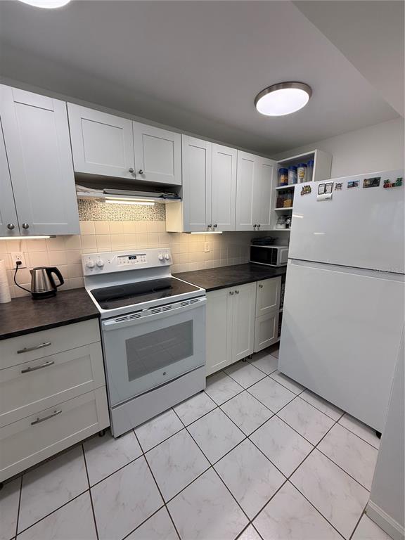 A kitchen features white cabinets, dark countertops, a white stove, and a white refrigerator — 1243 S MARTIN LUTHER KING JR AVENUE UNIT C303, CLEARWATER, FL