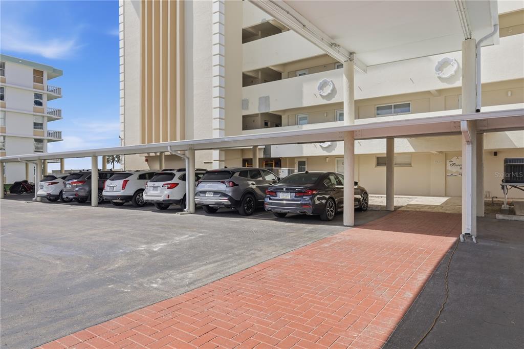 A covered parking area with several parked cars sits beside a multi-story apartment building — 1150 TARPON CENTER DRIVE UNIT 1G, VENICE, FL