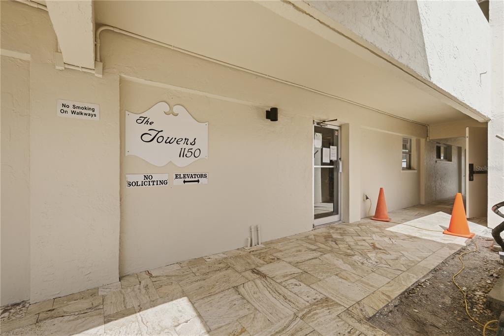 The exterior entrance of a building features a sign, tiled walkway, and orange traffic cones — 1150 TARPON CENTER DRIVE UNIT 1G, VENICE, FL