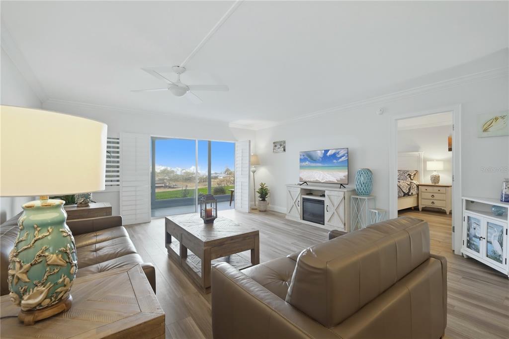 A living room features light wood flooring, a leather sofa, and a sliding glass door — 1150 TARPON CENTER DRIVE UNIT 1G, VENICE, FL