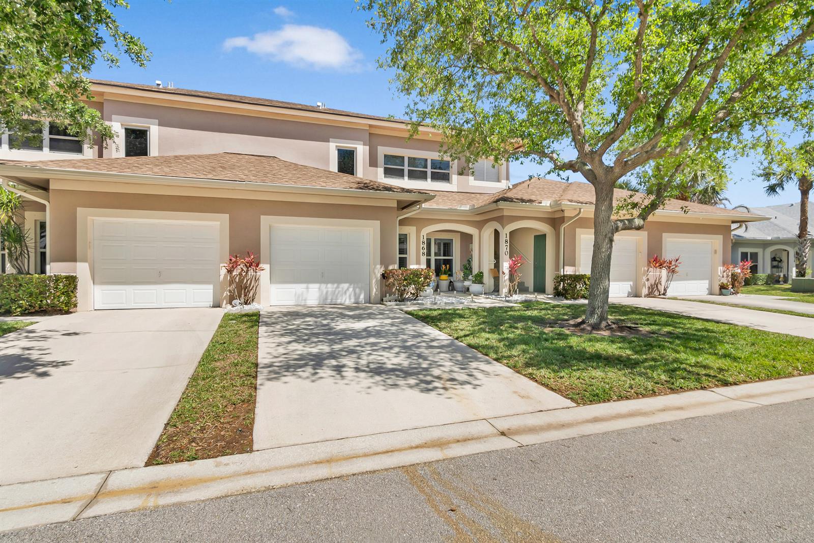 A two-story townhouse exterior features multiple garage doors, concrete driveways, and a large shade tree — 1868 E Sanderling Lane, Fort Pierce FL 34982, FORT PIERCE, FL