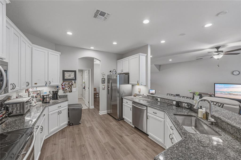 A kitchen features white cabinets, granite countertops, stainless steel appliances, and wood-look flooring — 1444 CYPRESS VIEW LANE, LAKELAND, FL