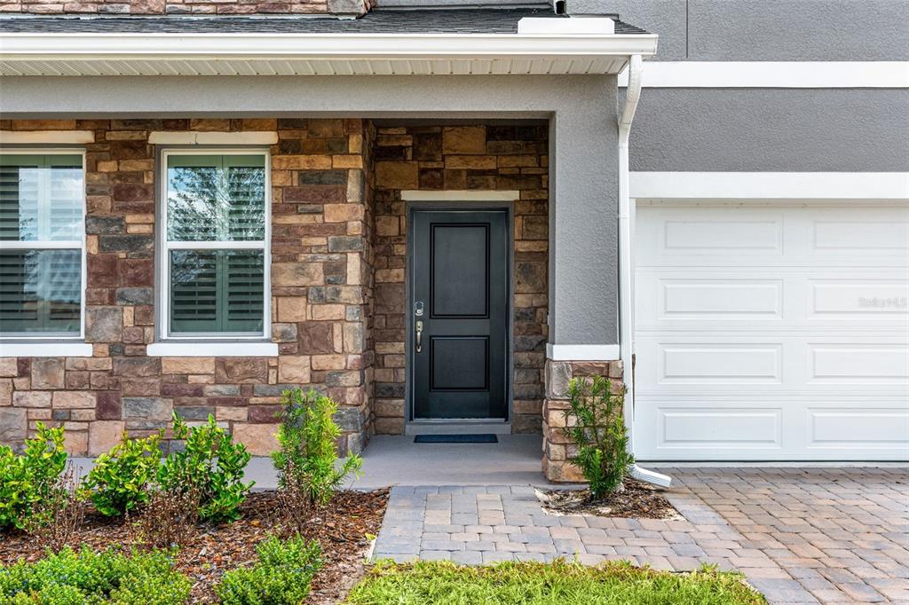 A stone-veneer exterior features a black front door, a white garage door, and landscaping — 1359 WOODLINE DRIVE, DELAND, FL