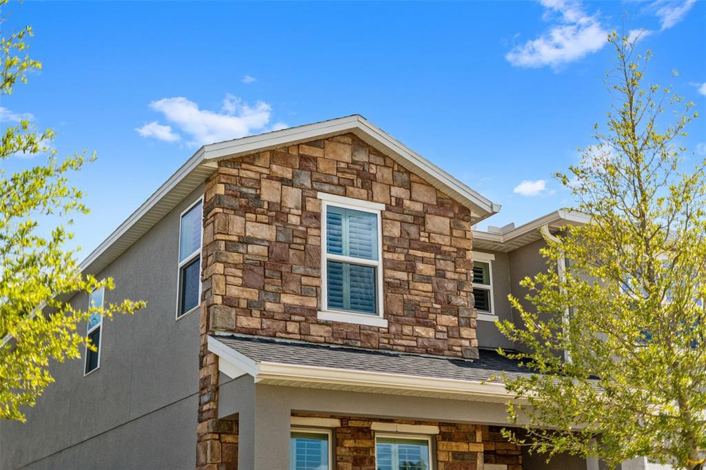 A two-story house exterior features gray stucco walls, stone veneer accents, and white-trimmed windows — 1359 WOODLINE DRIVE, DELAND, FL