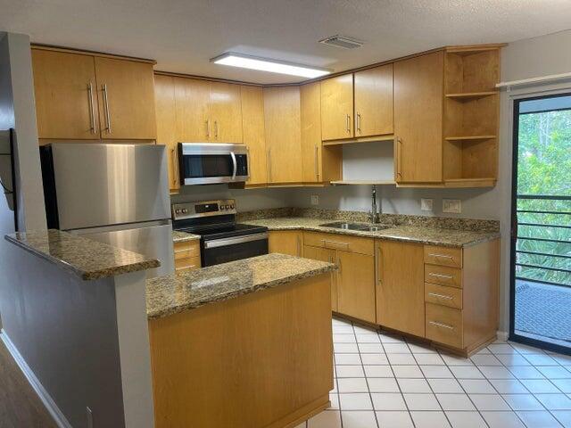 A kitchen with light wood cabinets, granite countertops, stainless steel appliances, and tile flooring — 4237 Oak Terrace Drive, FL 33463, FL