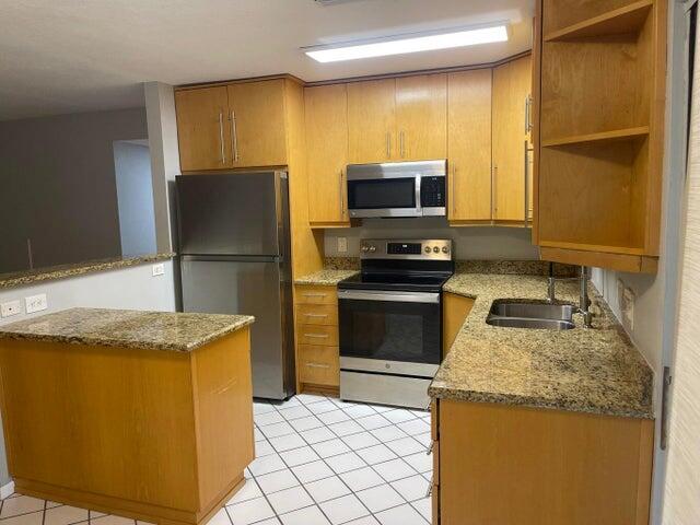 A kitchen features light wood cabinets, granite countertops, stainless steel appliances, and white tile flooring — 4237 Oak Terrace Drive, FL 33463, FL