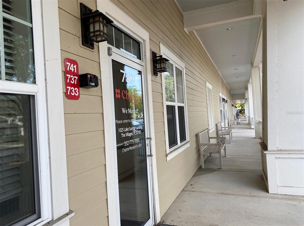 A covered outdoor walkway features light-colored siding, multiple windows, wall-mounted lanterns, and several wooden benches — 737 COUNTY ROAD 466, LADY LAKE, FL