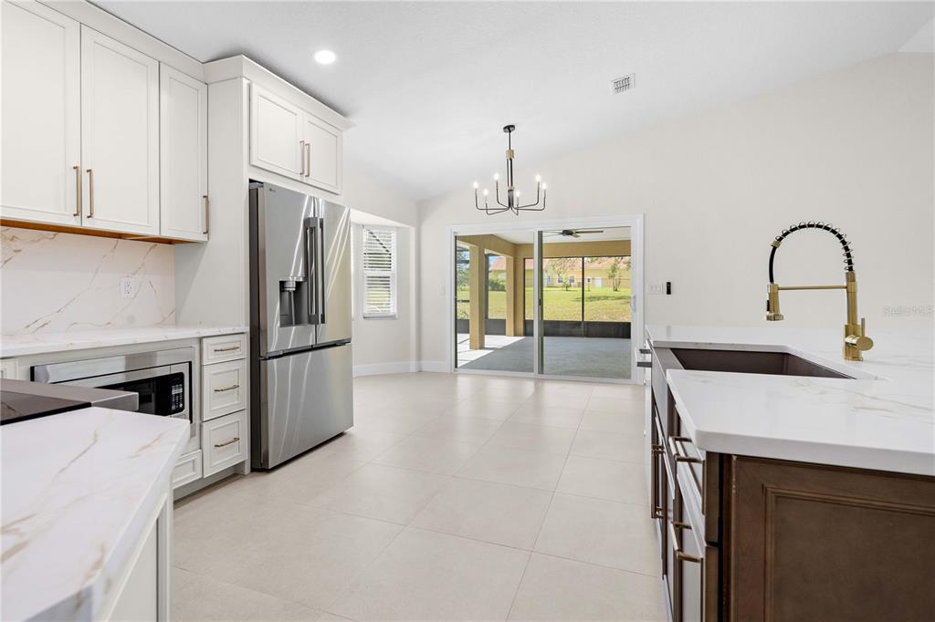 A modern kitchen features white cabinetry, a stainless steel refrigerator, and a gold-toned faucet — 9086 GROVE ROAD, BROOKSVILLE, FL