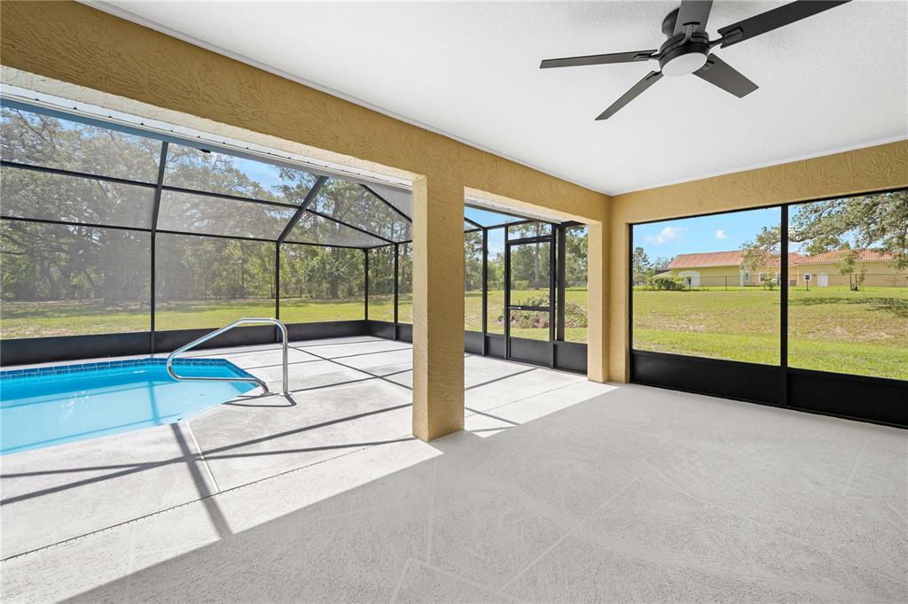 A covered patio with a ceiling fan overlooks a screened-in swimming pool and grassy yard — 9086 GROVE ROAD, BROOKSVILLE, FL