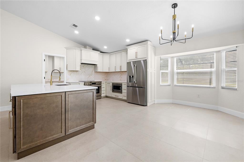 A modern kitchen features white cabinets, a brown island, stainless steel appliances, and tile flooring — 9086 GROVE ROAD, BROOKSVILLE, FL