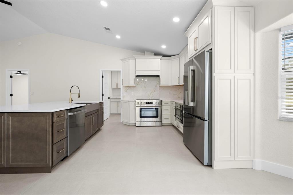 A modern kitchen features white cabinets, a dark island, stainless steel appliances, and tile flooring — 9086 GROVE ROAD, BROOKSVILLE, FL