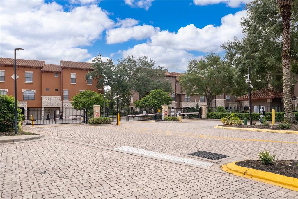 A gated entrance with a paved driveway leads to multi-story apartment buildings — 6141 METROWEST BOULEVARD UNIT 305, ORLANDO, FL