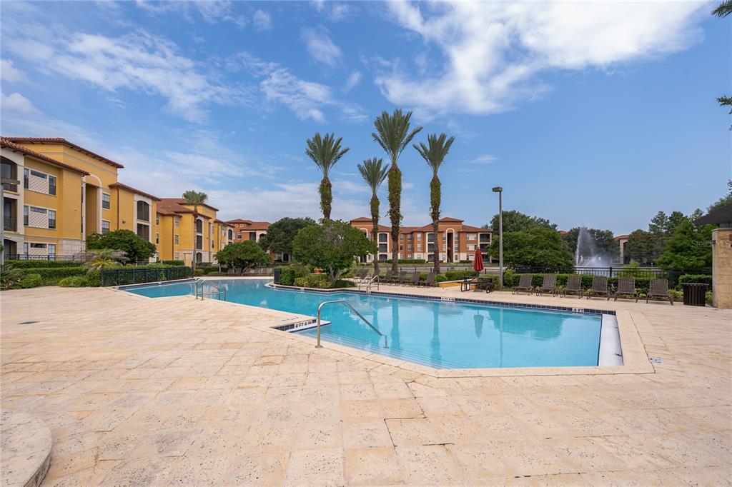A swimming pool with lounge chairs and palm trees sits in front of apartment buildings — 6141 METROWEST BOULEVARD UNIT 305, ORLANDO, FL
