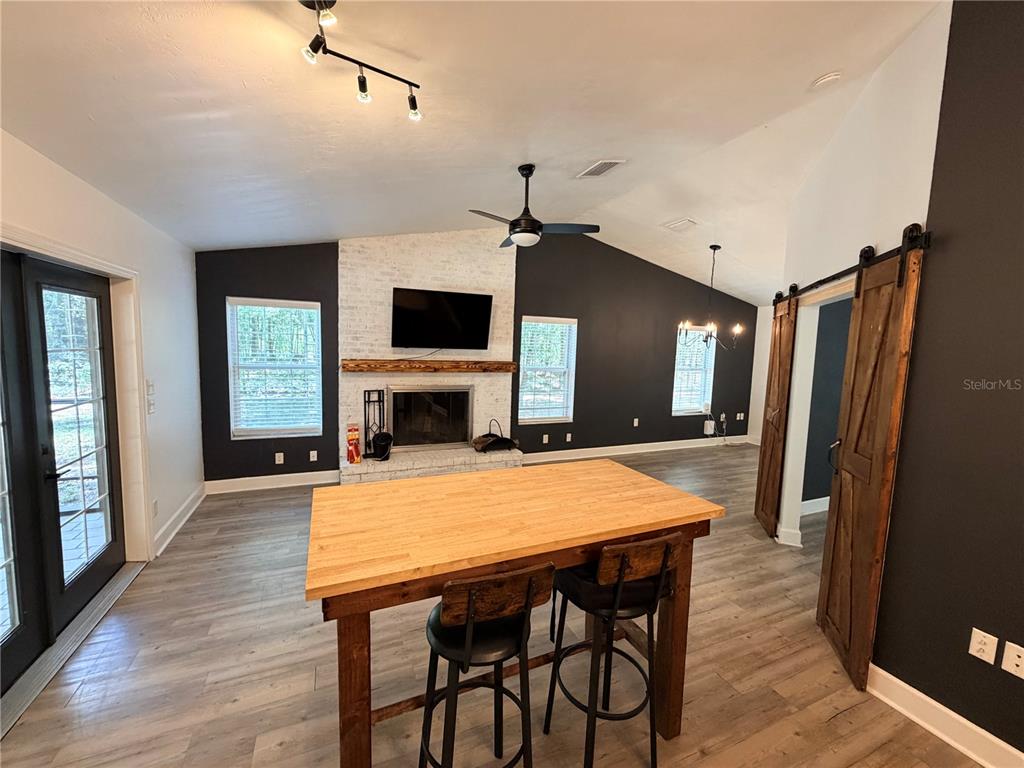 A living room features a brick fireplace, dark accent walls, wood-look flooring, and a kitchen island — 5309 NE 60TH AVENUE, HIGH SPRINGS, FL