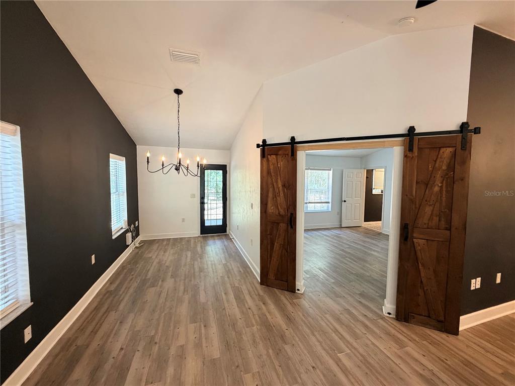 A room with wood-look flooring, a dark accent wall, and sliding barn doors — 5309 NE 60TH AVENUE, HIGH SPRINGS, FL